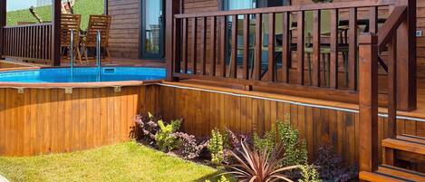 Eine Holzterrasse mit Pool, umgeben von einem gepflegten Rasen und diversen Pflanzen.