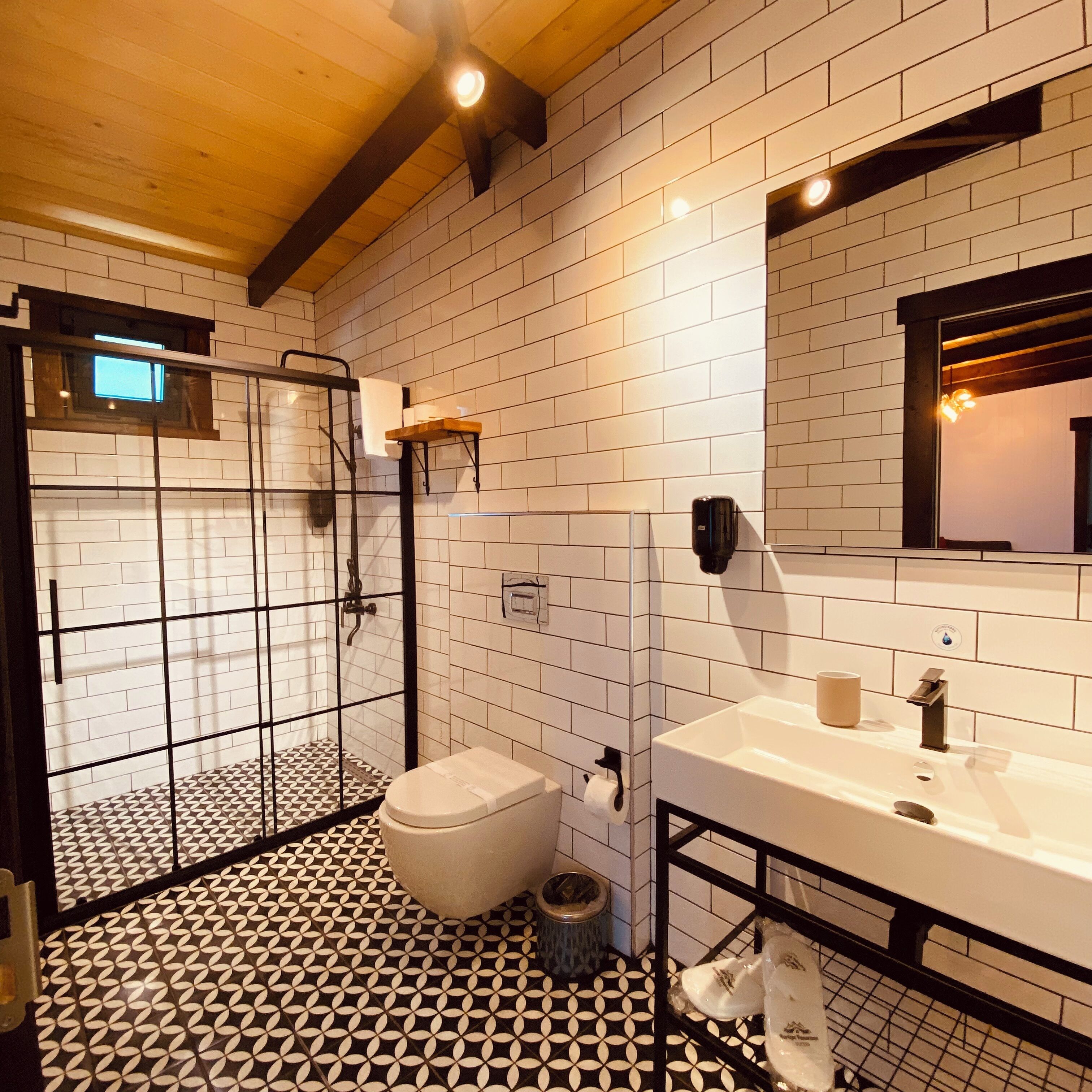 Un baño con suelo de baldosas blancas, inodoro blanco, lavabo con espejo y zona de ducha con puertas de cristal.