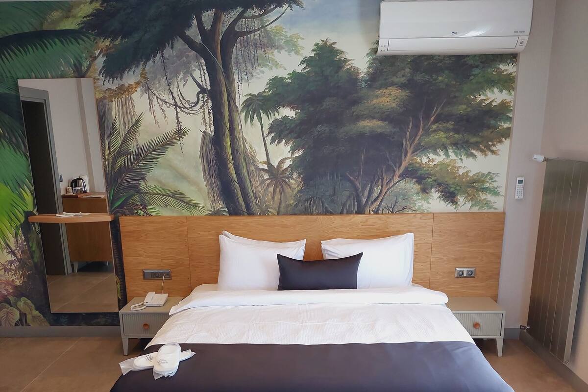 Une chambre d’hôtel avec un grand lit, une table de chevet, un bureau et une fresque murale représentant une scène de forêt.