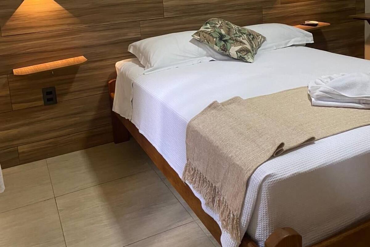 Una cama bien hecha con cabecera de madera, dos lámparas de pared y una mesita de noche.
