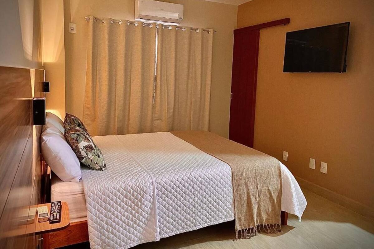 Un dormitorio con una cama, televisor, cortina y aire acondicionado instalado en la pared.