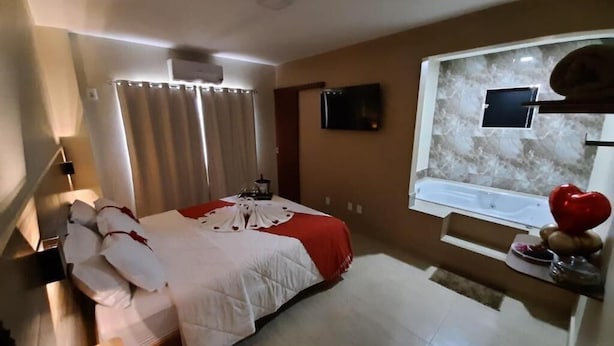 Ein Schlafzimmer mit einem Bett, Vorhängen, einem Fernseher, einem Fenster und einem roten Dekoelement.
