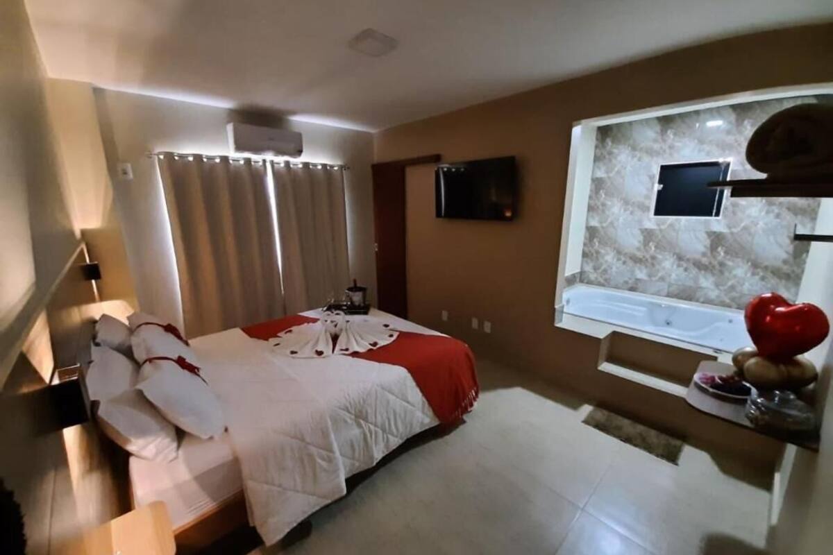 Un dormitorio con cama, cortinas, televisión, ventana y un adorno rojo.