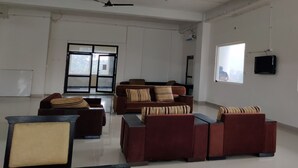 A spacious room with a large window, ceiling fans, and a flat-screen TV mounted on the wall. - Abuzz Oxfordcaps Dehradun - Campus Accommodation (Dehradun)