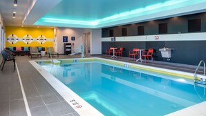 Ein Schwimmbecken mit gefliestem Boden, ein Umkleideraum mit gelber Wand und einem Schild sowie rote Stühle in der Nähe des Pools.