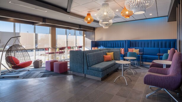 Ein moderner Lounge-Bereich mit einem blauen Sofa, roten und violetten Sesseln und hängenden Pendelleuchten.