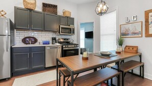 Une cuisine moderne avec des meubles de couleur sombre, un réfrigérateur en acier inoxydable, un four à micro-ondes et une cuisinière. On y trouve une table à manger en bois avec des bancs, un luminaire suspendu et un panier posé sur les meubles.