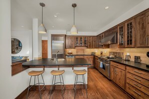 A modern kitchen with wooden cabinets, a large island with bar stools, stainless steel appliances, and pendant lighting. - Ballard 203 North - 2Bd, 2.5Ba - Sleeps 4 - Downtown Condo + Mountain Views (Telluride)