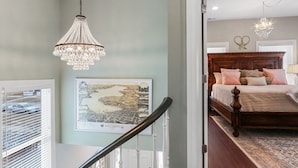Een slaapkamer met een groot bed, een kroonluchter en een ingelijst schilderij aan de muur.