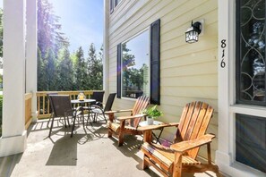 Una terraza de madera con sillas Adirondack y una pequeña mesa, una planta en maceta y el número 816 visible.