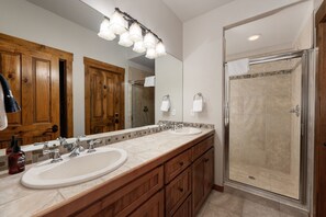 Une salle de bain avec deux lavabos, des meubles en bois, un grand miroir et une douche à l’italienne.