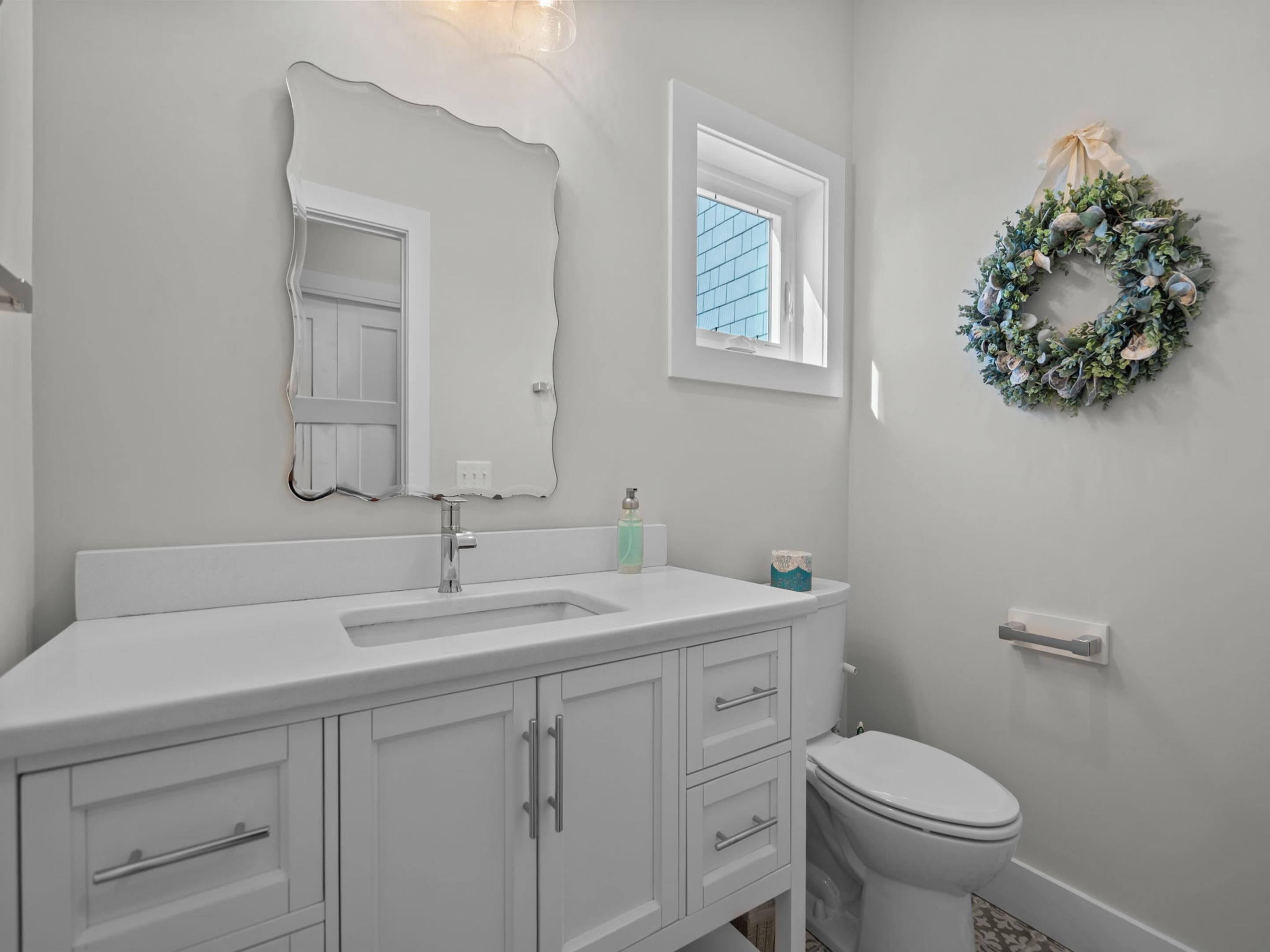 A bathroom with a white sink, a mirror, a toilet, and a window.