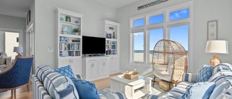 A spacious living room with a large sofa, a television, and a bookshelf.