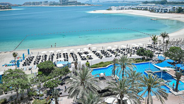 A resort with a large pool, beach area, and multiple lounge chairs. - Palm Jumeirah's Spectacular Ocean-View Apartment - NBT (Dubai)