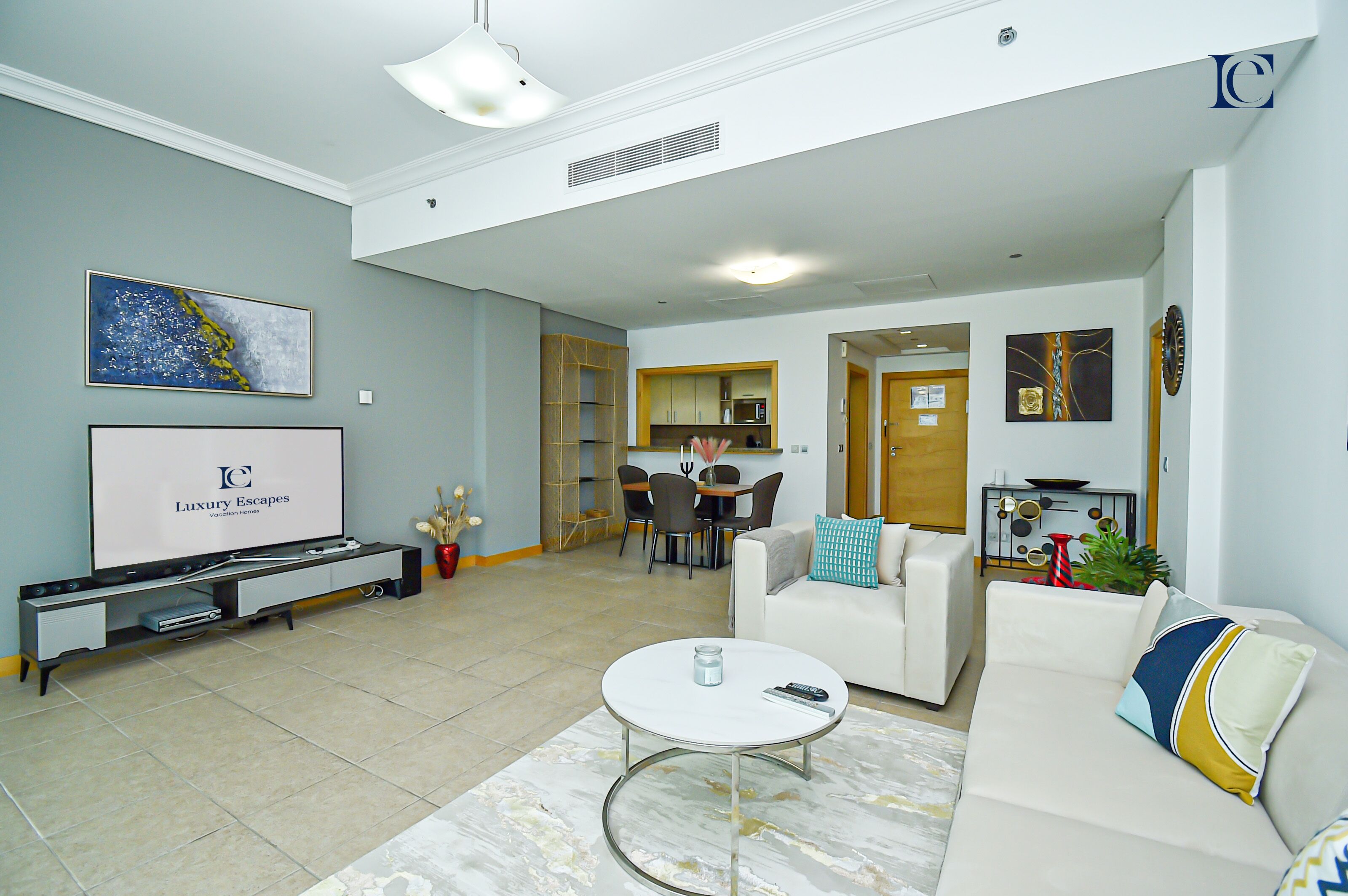Uma sala de estar ampla, com televisão de tela plana, um sofá branco, uma mesa de centro e um espaço de jantar com cadeiras e mesa.