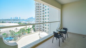A balcony with a view of a city skyline, a pool, and palm trees. - Palm Jumeirah's Spectacular Ocean-View Apartment - NBT (Dubai)