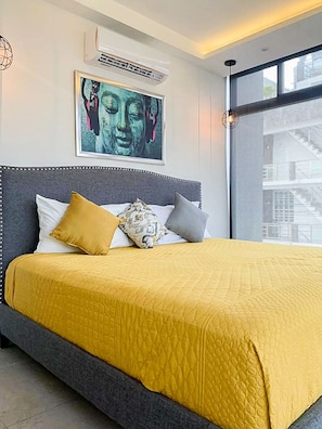 Une chambre moderne avec un grand lit, une vue sur la ville et un tableau représentant Bouddha accroché au mur.