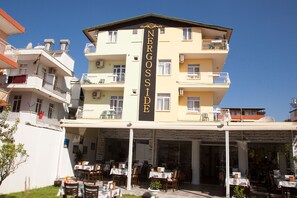 Un hotel de varios pisos con un cartel llamativo que dice “NERGOSSI DE”. Cuenta con asientos al aire libre con mesas y sillas, y balcones en cada planta.