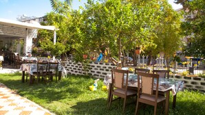 An outdoor seating area with tables and chairs, surrounded by greenery and a stone wall. - Nergos Side Hotel (Manavgat)