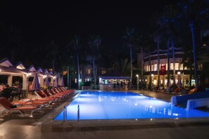 A swimming pool with lounge chairs and umbrellas, surrounded by palm trees and a building with a bar area. - Nergos Side Hotel (Manavgat)