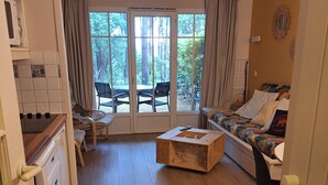 A compact living space with a kitchenette, a sofa, a dining table, and a large window with a view of trees.