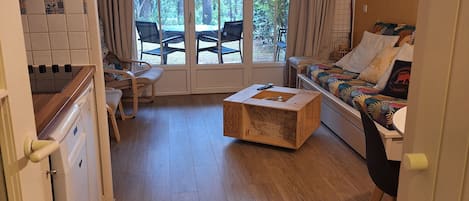 A compact living space with a kitchenette, a sofa, a dining table, and a large window with a view of trees.