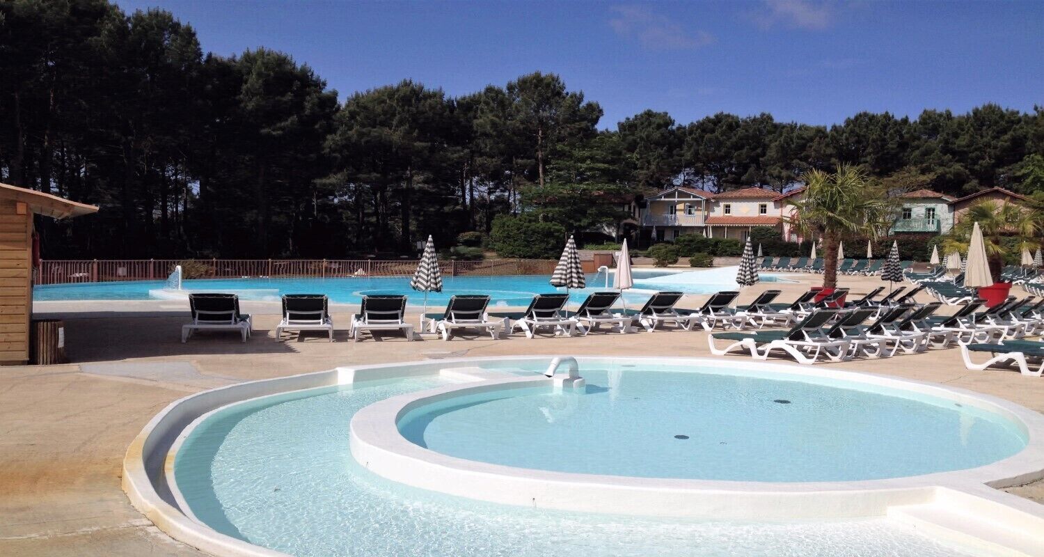 A swimming pool with lounge chairs and umbrellas, surrounded by trees and buildings.