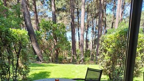 A patio with a round table and chairs, surrounded by a lush garden and tall trees.