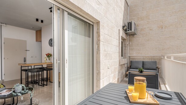 En balkon med et bord dækket med drikkevarer, en sofa samt et spiseområde med stole og bord.