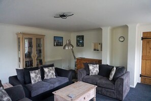 A living room with two sofas, a coffee table, a bookshelf, and a clock on the wall.