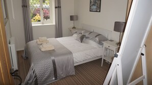 A neatly arranged bedroom with a bed, bedside tables, a window with curtains, a radiator, and a painting on the wall.