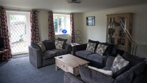 A living room with two sofas, a coffee table, a bookshelf, and a window with curtains.