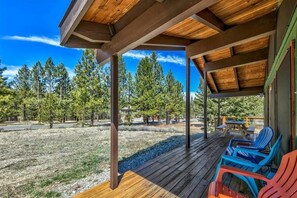 Un espacio al aire libre techado con terraza de madera, sillas y vista a árboles.