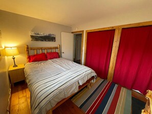 Un dormitorio con cama, mesita de noche, lámpara, puerta y cortina roja.