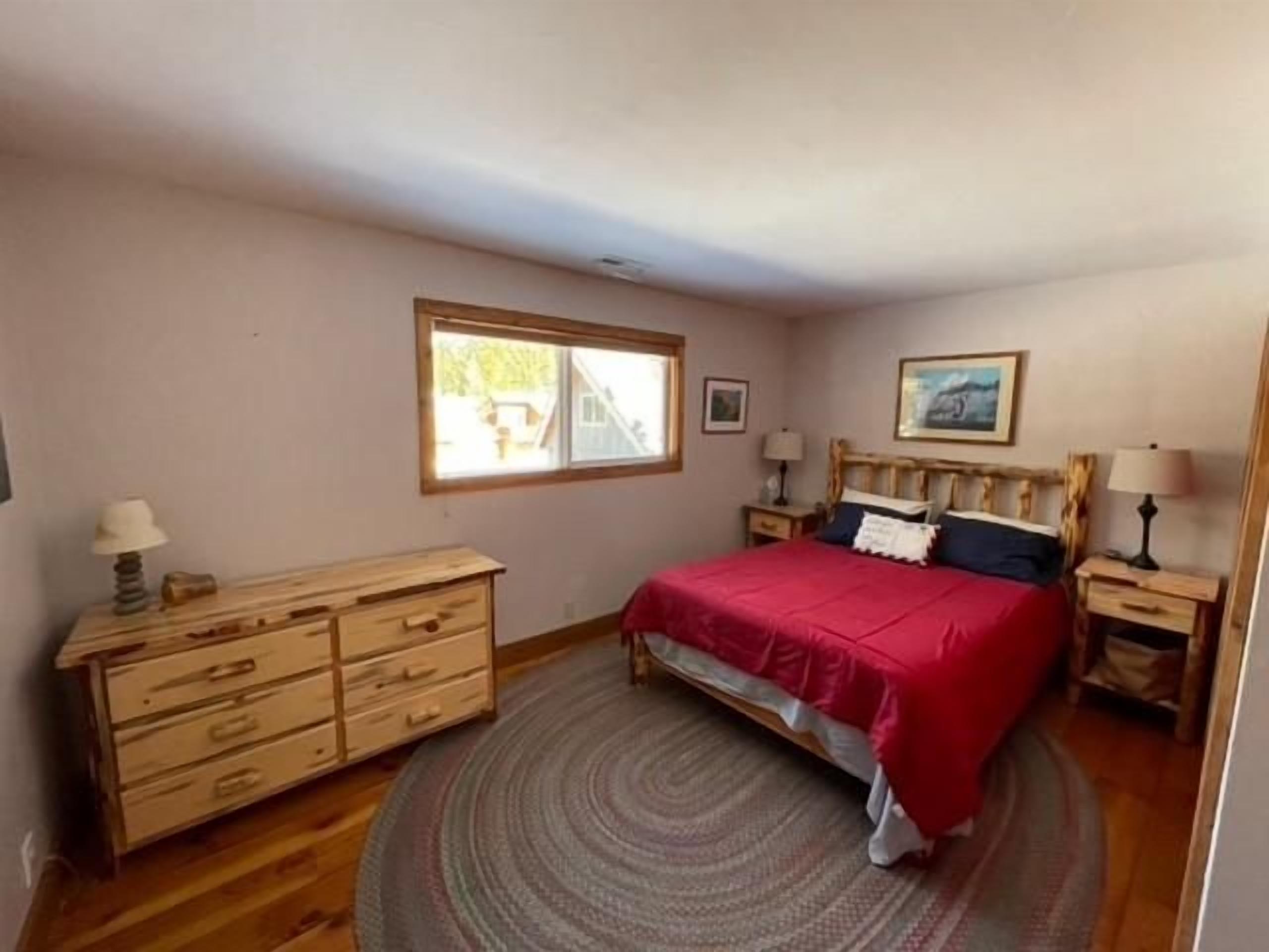 Una camera da letto con un letto, una cassettiera, due comodini, una finestra e un quadro appeso al muro.