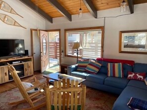 Una sala de estar con una televisión, un sofá azul, un sillón mecededor y una mesa de madera.