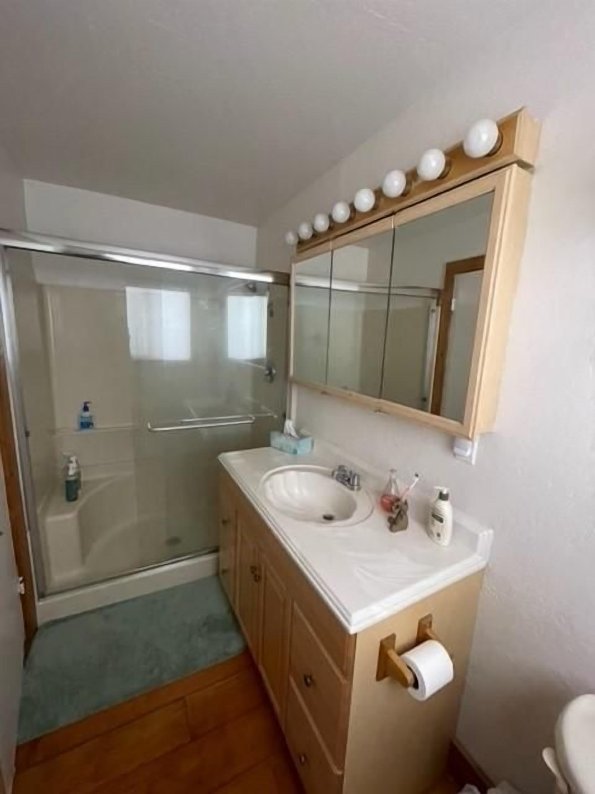 Un baño con cabina de ducha de vidrio, un lavamanos con espejo y un inodoro.