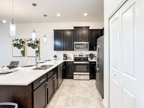 A modern kitchen with dark cabinets, stainless steel appliances, and a marble countertop.