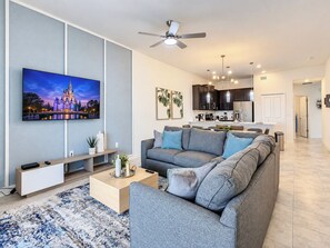 Una sala moderna con un sofá gris, un televisor de pantalla plana y un ventilador de techo.
