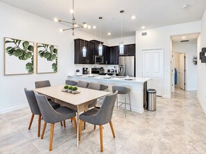 Una cocina moderna con armarios oscuros, una isla central y un comedor con mesa y sillas.