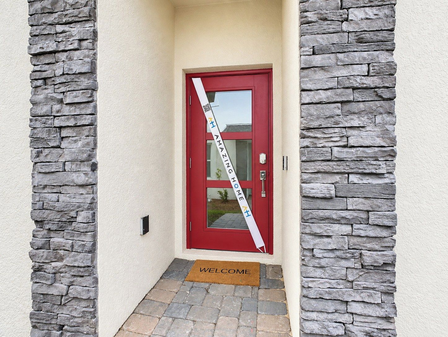 A red door with a 'WELCOME' mat and a 'AMAZING HOME' banner.