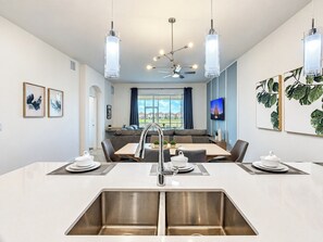Una cocina moderna con una isla central, pileta de acero inoxidable y lámparas colgantes.