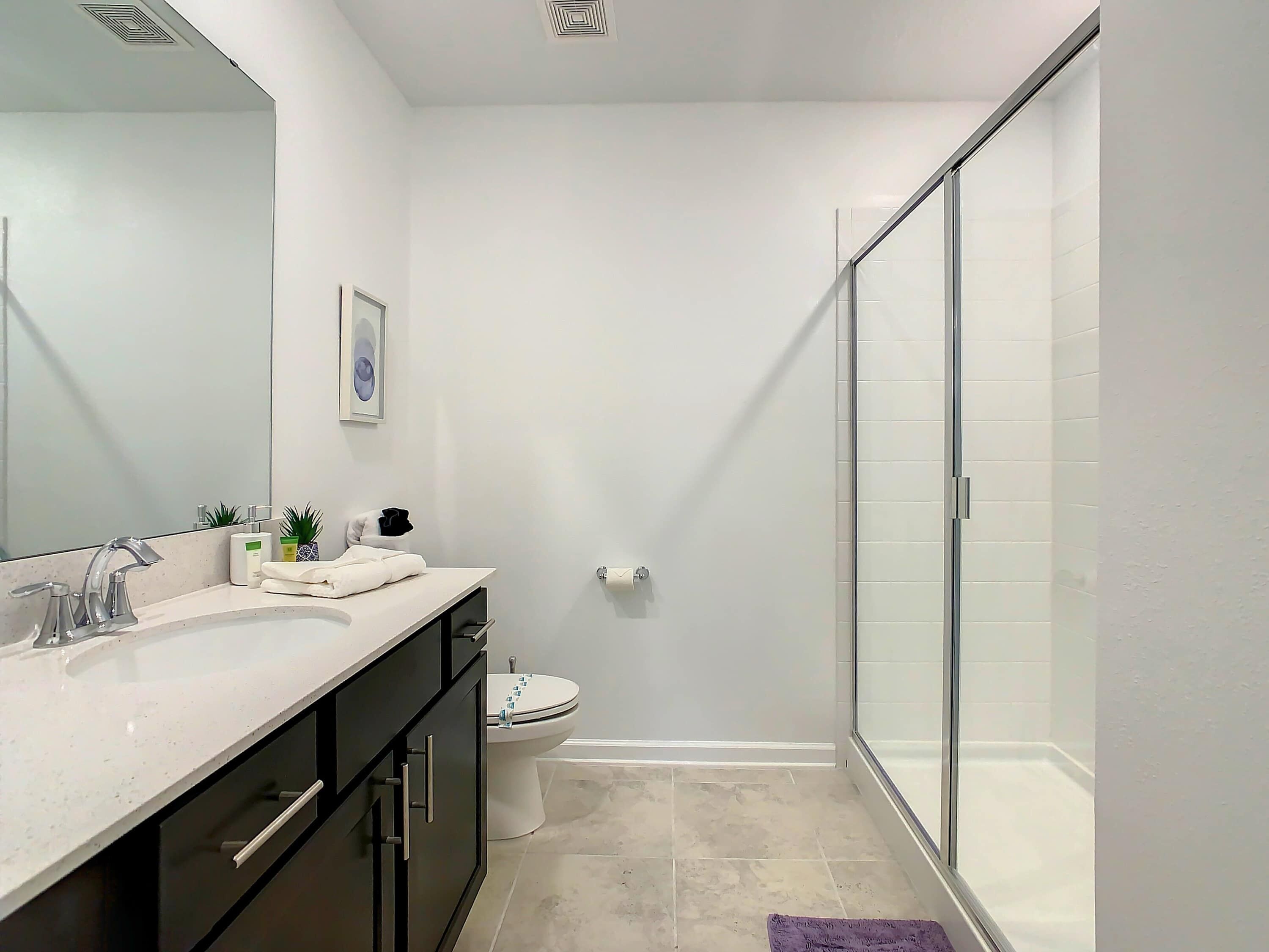 A modern bathroom with a large mirror, a sink, a toilet, and a glass shower enclosure.