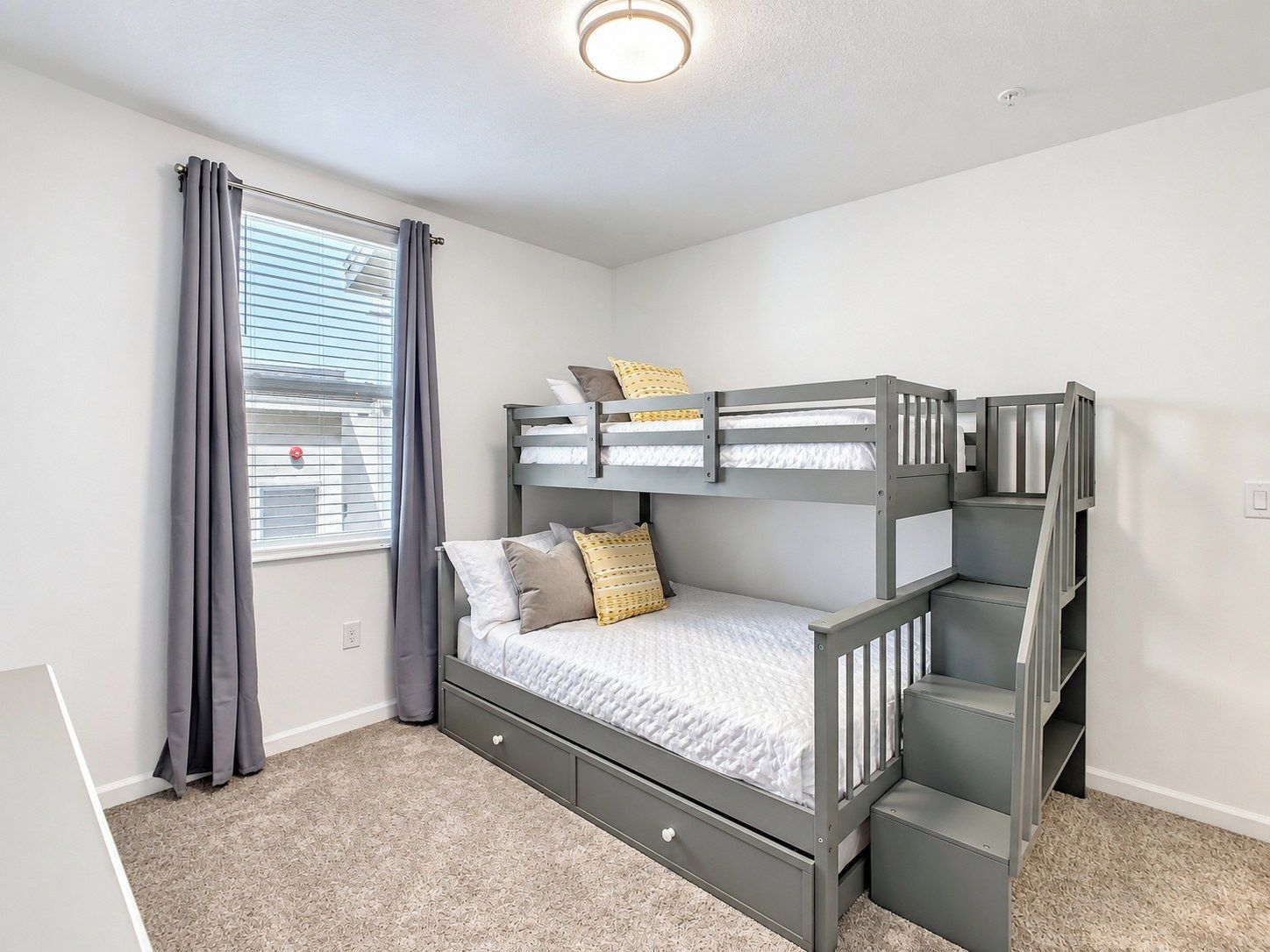 A bunk bed room with a window, curtains, and a carpeted floor.