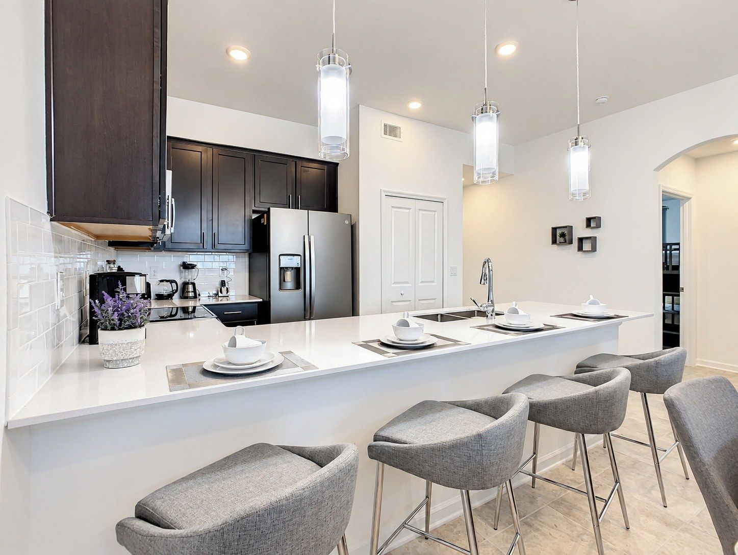 Cozinha moderna com ilha central, banquetas, eletrodomésticos de aço inoxidável e iluminação pendente.