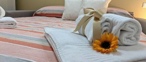 Een opgemaakt bed met gestreepte lakens, een opgerolde witte handdoek, een decoratieve strik en een zonnebloem.