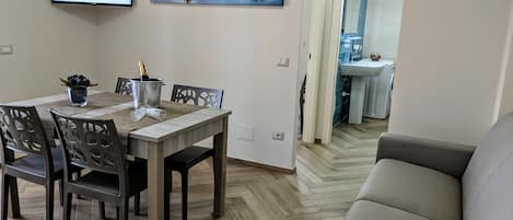 Un comedor con mesa de madera, sillas y una pantalla de televisión. En la pared, un cuadro de un lago y montañas.