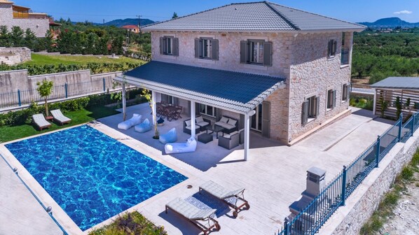 A two-story stone house with a swimming pool, outdoor seating, and a covered patio.