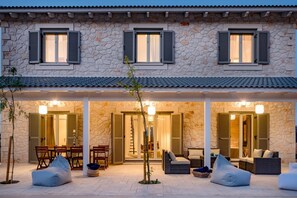 Un bâtiment en pierre doté de trois portes ouvertes qui donnent sur un patio abrité, aménagé avec des sièges d’extérieur.