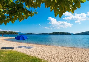 A beach with a blue umbrella, clear blue water, and distant hills.